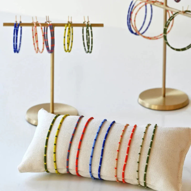 LADDER’s colorful beaded bracelets displayed on a white cushion and gold jewelry stands.