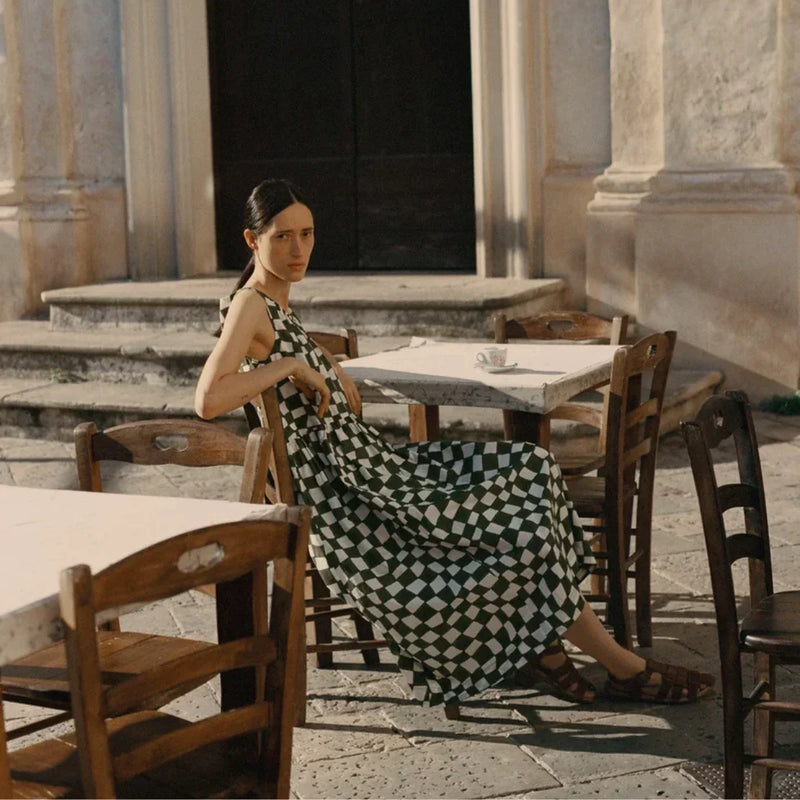 Woman wearing the TOAST green and ivory checkered maxi dress with brown leather sandals, styled at an outdoor café, available at LADDER.
