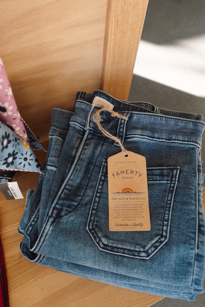 Folded blue jeans with a Faherty tag on a wooden surface