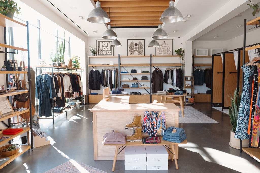 Modern sustainable women's curated clothing store interior with racks of clothes and a wooden display table.