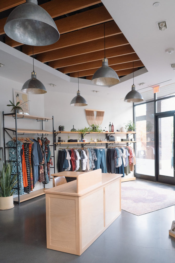 Modern sustainable curated clothing store interior with wooden display counters and hanging clothes.