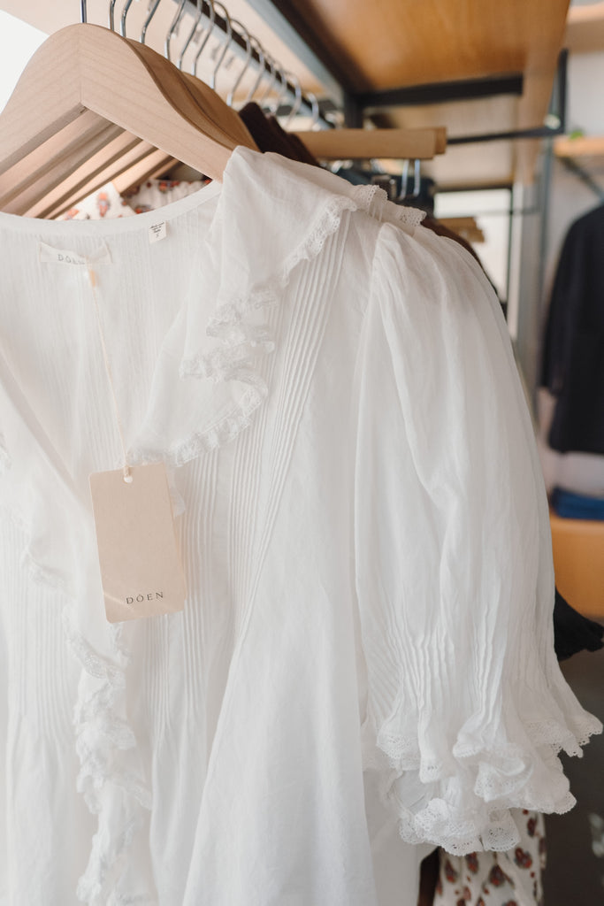 White lace top on a hanger with a visible DOEN tag in a store setting